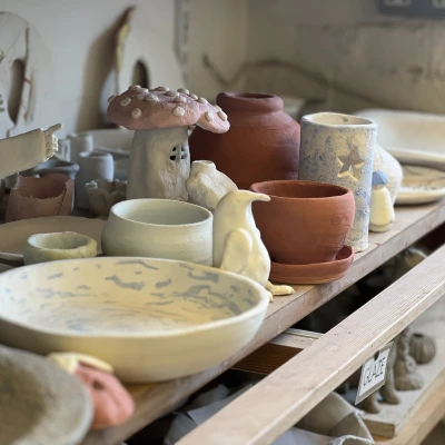 A shelf in a pottery studio, featuring several pottery works. Such as bowls, plates and sculptures.